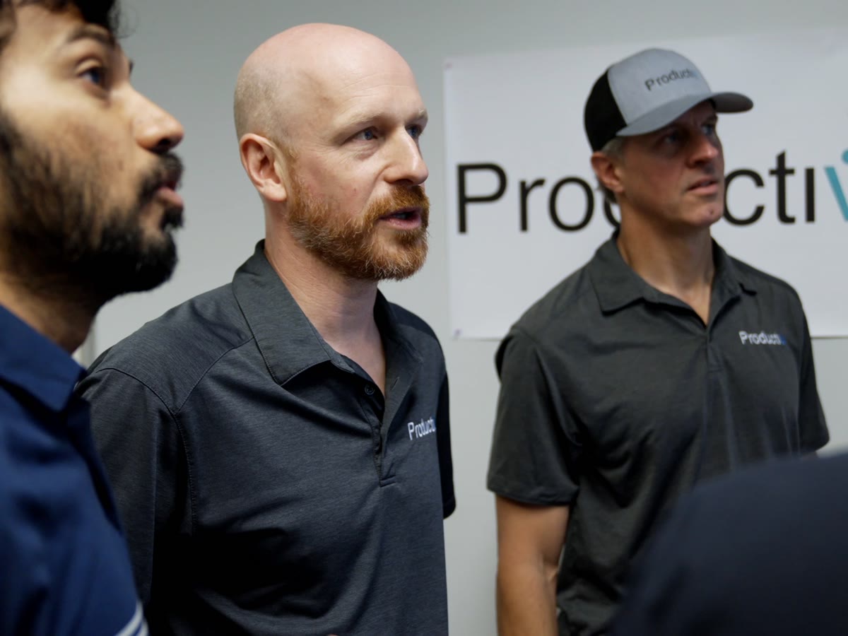 Productiv leadership on the warehouse floor in front of the Productiv sign