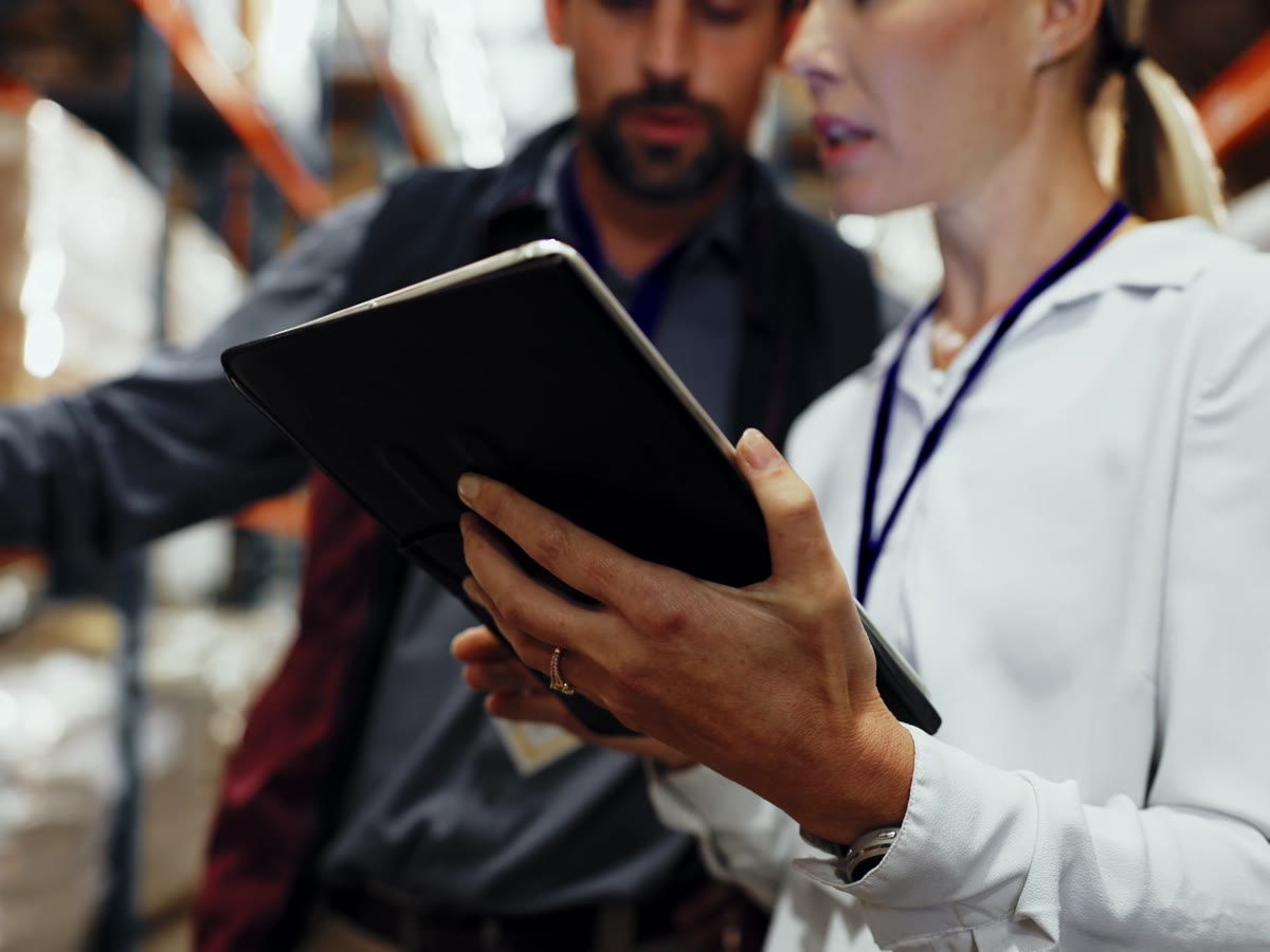 Two Productiv team members reviewing orders on a tablet between warehouse racks